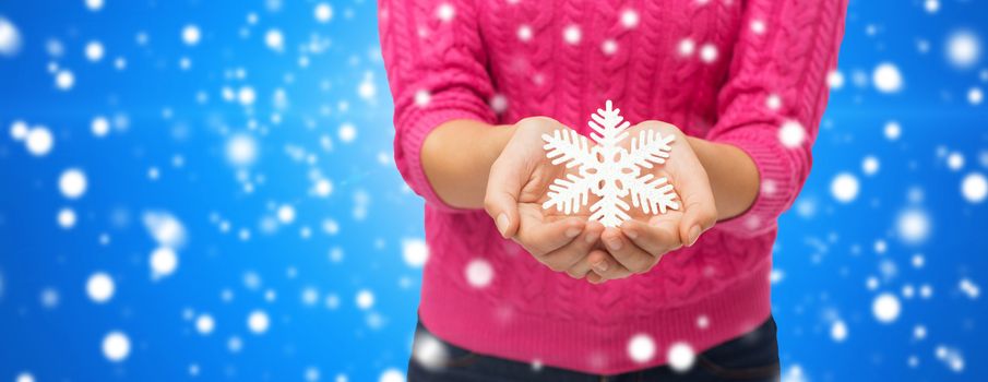 christmas, winter, holidays and people concept - close up of woman in pink sweater holding snowflake decoration over blue snowy background