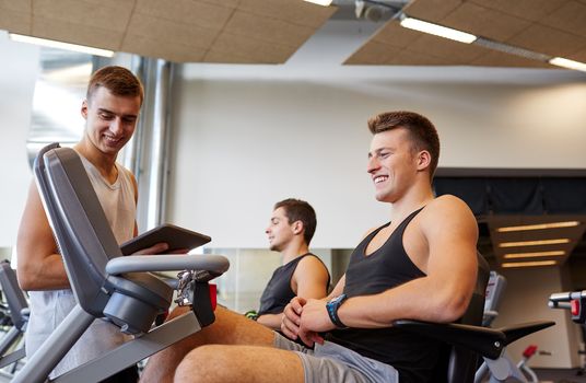 sport, fitness, equipment, technology and people concept - men with tablet pc computer exercising on gym machine