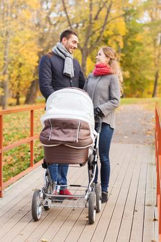 love, parenthood, family, season and people concept - smiling couple with baby pram in autumn park