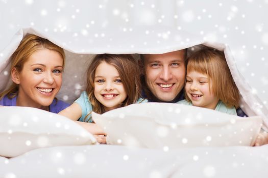 family, children, comfort, bedding and home concept - happy family with two kids under blanket over snowflakes background