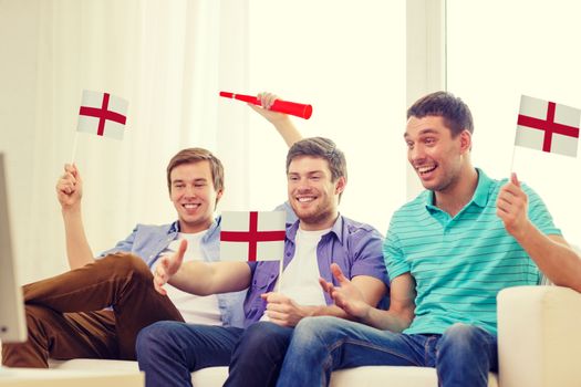 friendship, sports and entertainment concept - happy male friends with flags and vuvuzela supporting football team at home