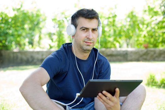 young man holding a tablet with headphones, outdoor