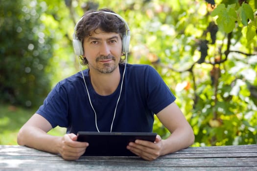 young man holding a tablet with headphones, outdoor