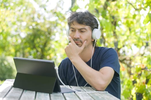 young man working with a tablet pc with headphones, outdoor