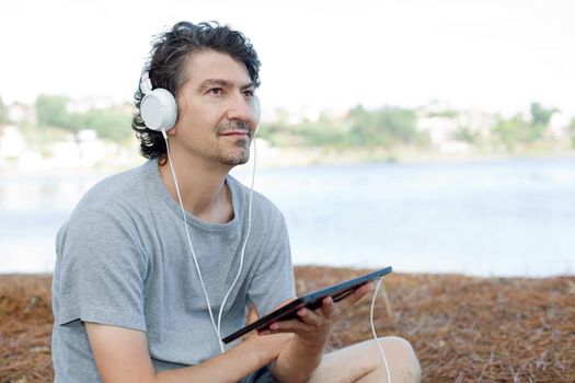 young man holding a tablet with headphones, at the beach