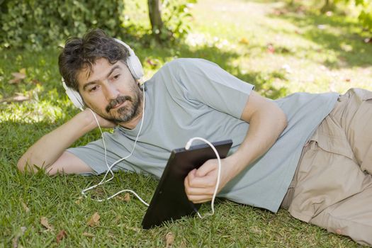 young man holding a tablet with headphones, outdoor