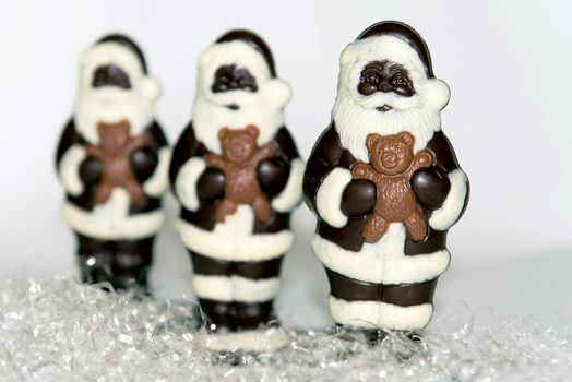 Close-up of a trio of chocolate santas on 'snow' with a whote background.