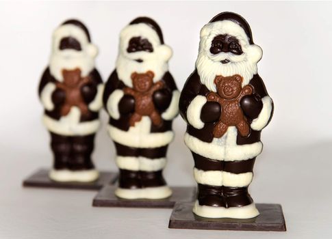 Close-up of a trio of chocolate santas on white.