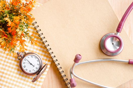 Stethoscope on Diary and vintage clock with flower on wooden background.