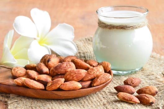 Almond milk in glass with almonds on sack background.