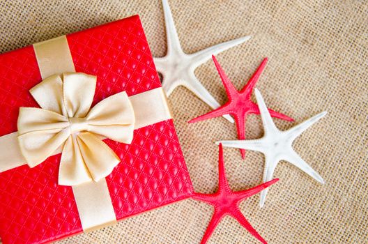 red gift box with gold ribbon and star fish on sack background