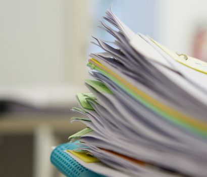 Pile of documents and blue file on desk at office.