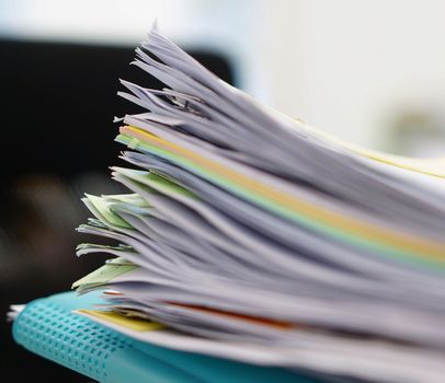 Pile of documents and blue file on desk at office.