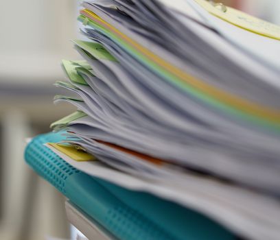 Pile of documents and blue file on desk at office.