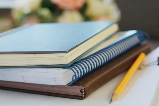 Three notebooks, stack of document and yellow pencil placed on table at office.