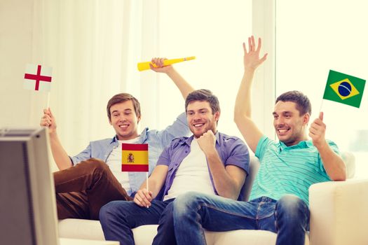 friendship, sports and entertainment concept - happy male friends with flags and vuvuzela supporting football team at home