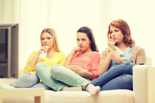 home, technology and friendship concept - three sad teenage girl watching tv at home and eating popcorn