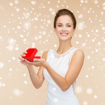 holidays, presents, wedding and happiness concept - smiling woman in white dress holding red gift box over beige background over beige background and snow