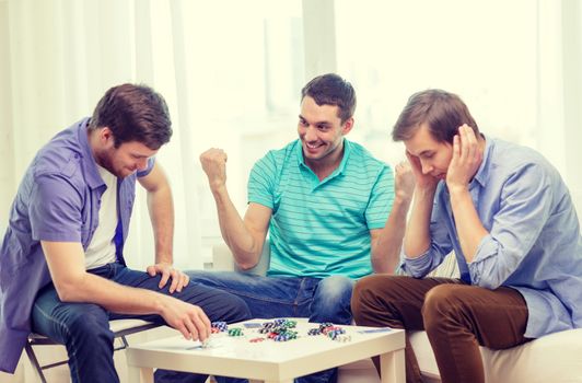 leisure, games and lifestyle concept - happy three male friends playing poker at home