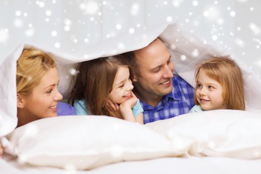 family, children, comfort, bedding and home concept - happy family with two kids under blanket over snowflakes background