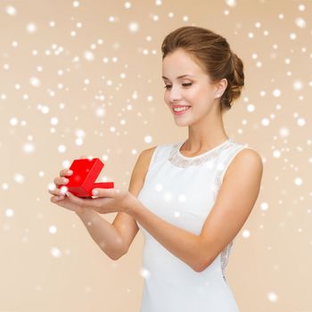 holidays, presents, wedding and happiness concept - smiling woman in white dress holding red gift box over beige background over beige background and snow