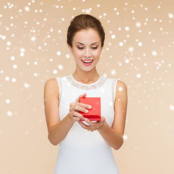 holidays, presents, wedding and happiness concept - smiling woman in white dress holding red gift box over beige background over beige background and snow