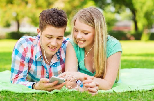 vacation, holidays, technology and friendship concept - smiling couple with smartphone and earphones lying on blanket in park