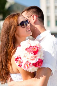 love, wedding, summer, dating and people concept - smiling couple wearing sunglasses with bunch of flowers hugging in city