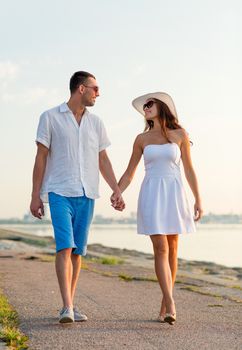 love, travel, tourism, summer and people concept - smiling couple on vacation wearing sunglasses and holding hands walking at seaside