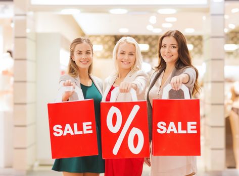 consumerism and people concept - happy young women holding shopping bags with sale and percentage sign in mall