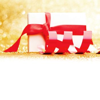 White gift box with red ribbon on golden glitter background
