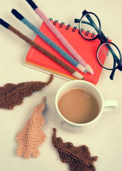 Romantic desk with ornament from handmade product, lily flower knit from white yarn, handbook, knitting pencil, coffee cup, glasses, beautifil craft