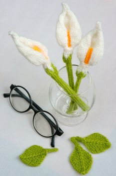 Romantic desk with ornament from handmade product, lily flower knit from white yarn, handbook, knitting pencil, coffee cup, glasses, beautifil craft
