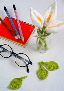 Romantic desk with ornament from handmade product, lily flower knit from white yarn, handbook, knitting pencil, coffee cup, glasses, beautifil craft