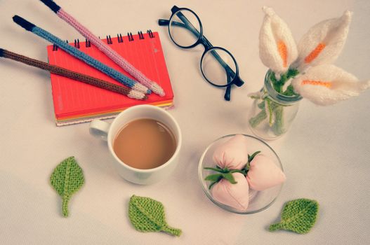 Romantic desk with ornament from handmade product, lily flower knit from white yarn, handbook, knitting pencil, coffee cup, glasses, beautifil craft