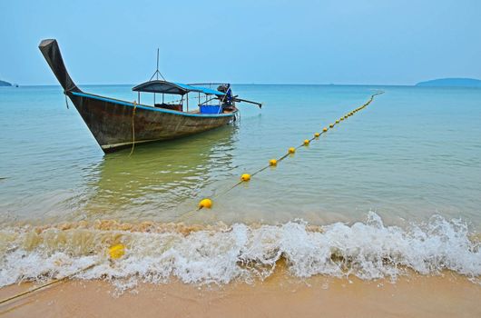 Traditional Thailand old vintage unpainted long tail boat without engine in transparent turquoise water crossed with yellow float buoys