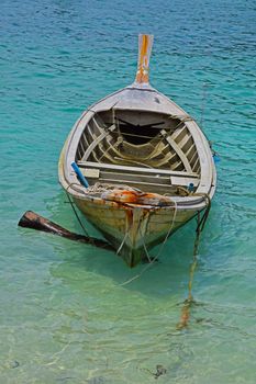 Traditional Thailand old vintage unpainted long tail boat without engine in transparent turquoise water
