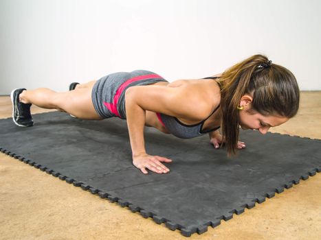 Photo of a beautiful young woman doing pushups in the gym.
