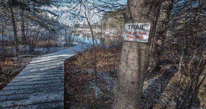 A walking trail warning sign on a tree advises of risk.  Foot path in winter woods. Fresh fallen snow, winter day.