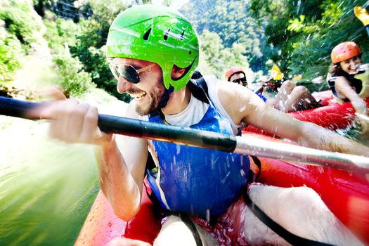 Excited male having fun, laughing on a rafting inflatable canoe being water attacked by a female from another boat.