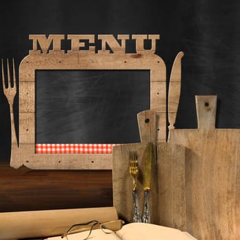 Empty blackboard with wooden frame and text Menu in the kitchen with cutting boards, silver cutlery, recipe book, eyeglasses and rolling pin. Template for food menu