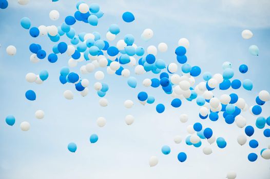 Balloons in white and two shades of blue on a cloudy sky background.
