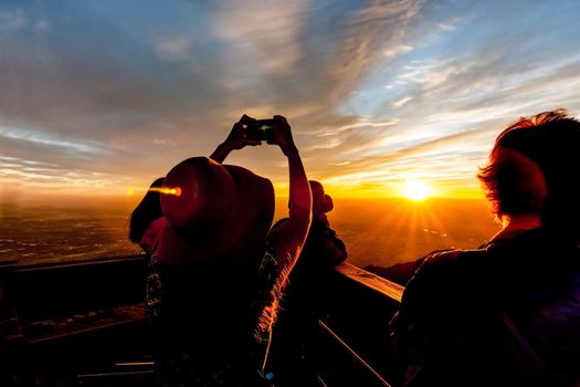 Silhouetted Tourists watch and photograph brilliant New Mexico sunset from Sandia Peak, Albuquerque, New Mexico, USA.