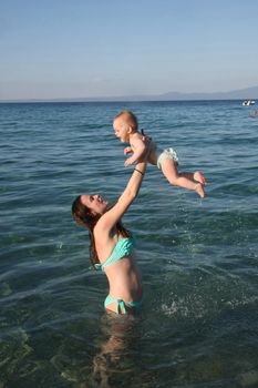 Mother playing with  her baby daughter  in the sea water