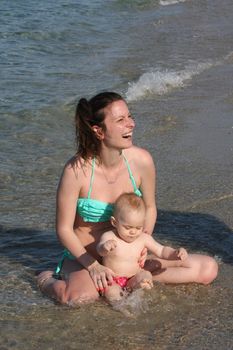 Mother with  her baby daughter sitting on the on the beach sand