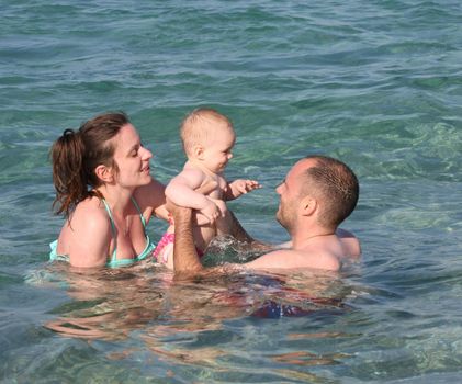 Mother and father with their baby girl enjoying swimming in the sea