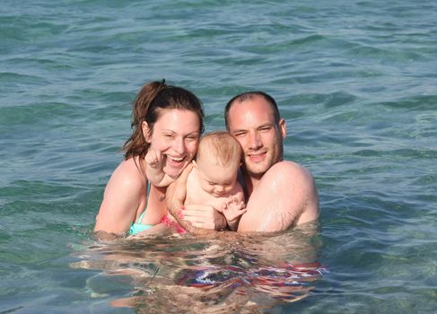 Mother and father with their baby girl enjoying swimming in the sea 
