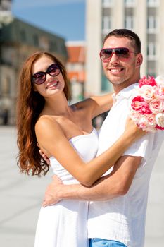 love, wedding, summer, dating and people concept - smiling couple wearing sunglasses with bunch of flowers hugging in city