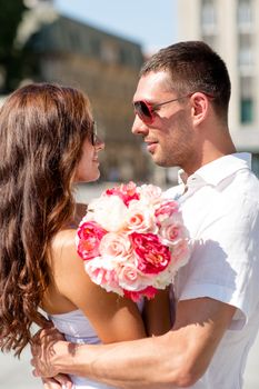 love, wedding, summer, dating and people concept - smiling couple wearing sunglasses with bunch of flowers hugging in city