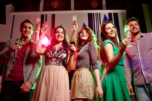 party, holidays, celebration, nightlife and people concept - smiling friends in party caps with glasses of champagne in club